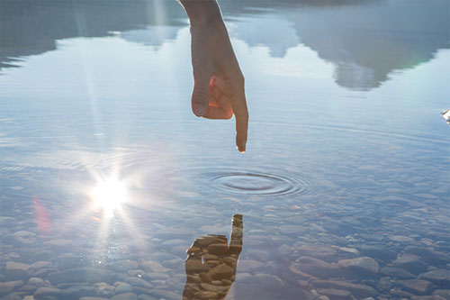 Refection of a persons finger rippling the water - creativity