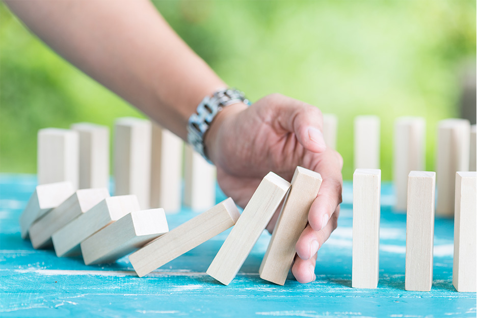 A hand preventing wooden dominos falling, symbolising stopping addictive behaviours